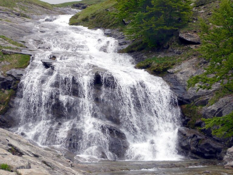 Cascata alta in Italia, con acqua che scorre vigorosamente tra le rocce, immersa nella natura.